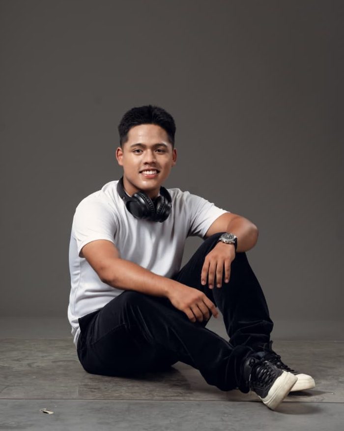Portrait of Kaustuv Batajoo in a white T-shirt, with headphones around the neck